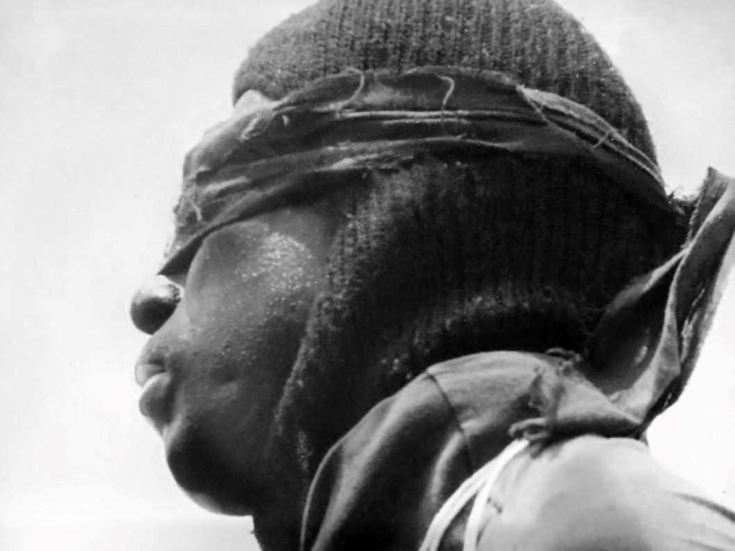 Black & white photo by Maya Vulinovic. A man in a hat is blindfolded and viewed in profile. 